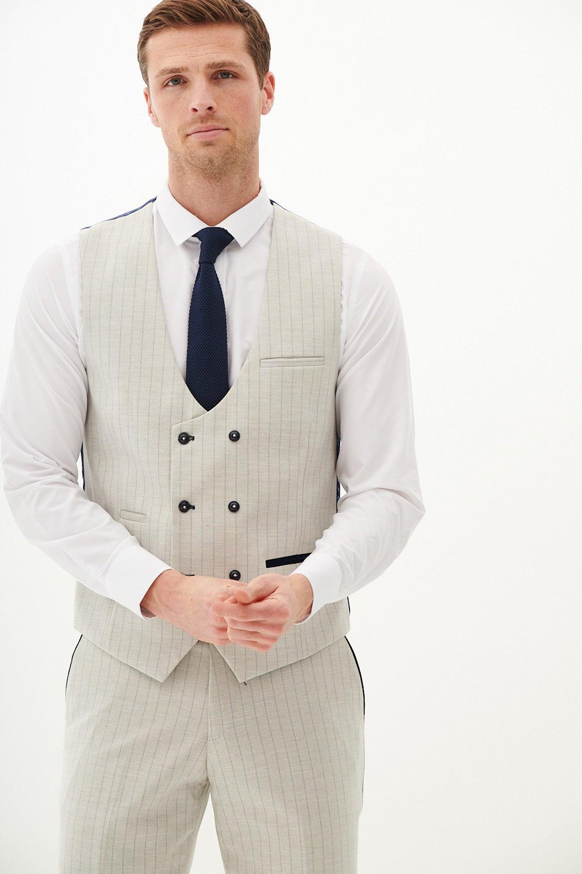 A man wears the Marc Darcy GRANT Stone Double Breasted Pinstripe Waistcoat with matching pants, a white dress shirt, and a dark navy tie, standing against a plain white background.
