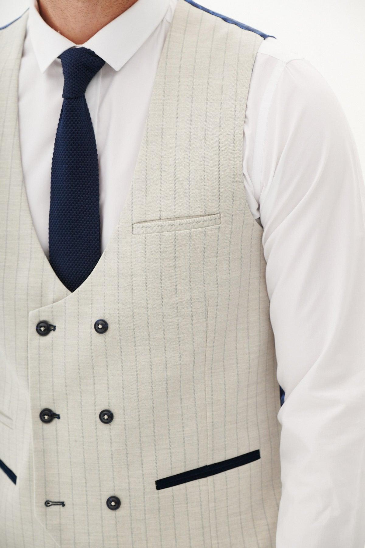 A man wears the Marc Darcy GRANT Stone Double Breasted Pinstripe Waistcoat over a white shirt with a navy tie. The slim fit waistcoat has dark buttons, a chest pocket, and two dark-trimmed pockets. He is cropped at the shoulders.