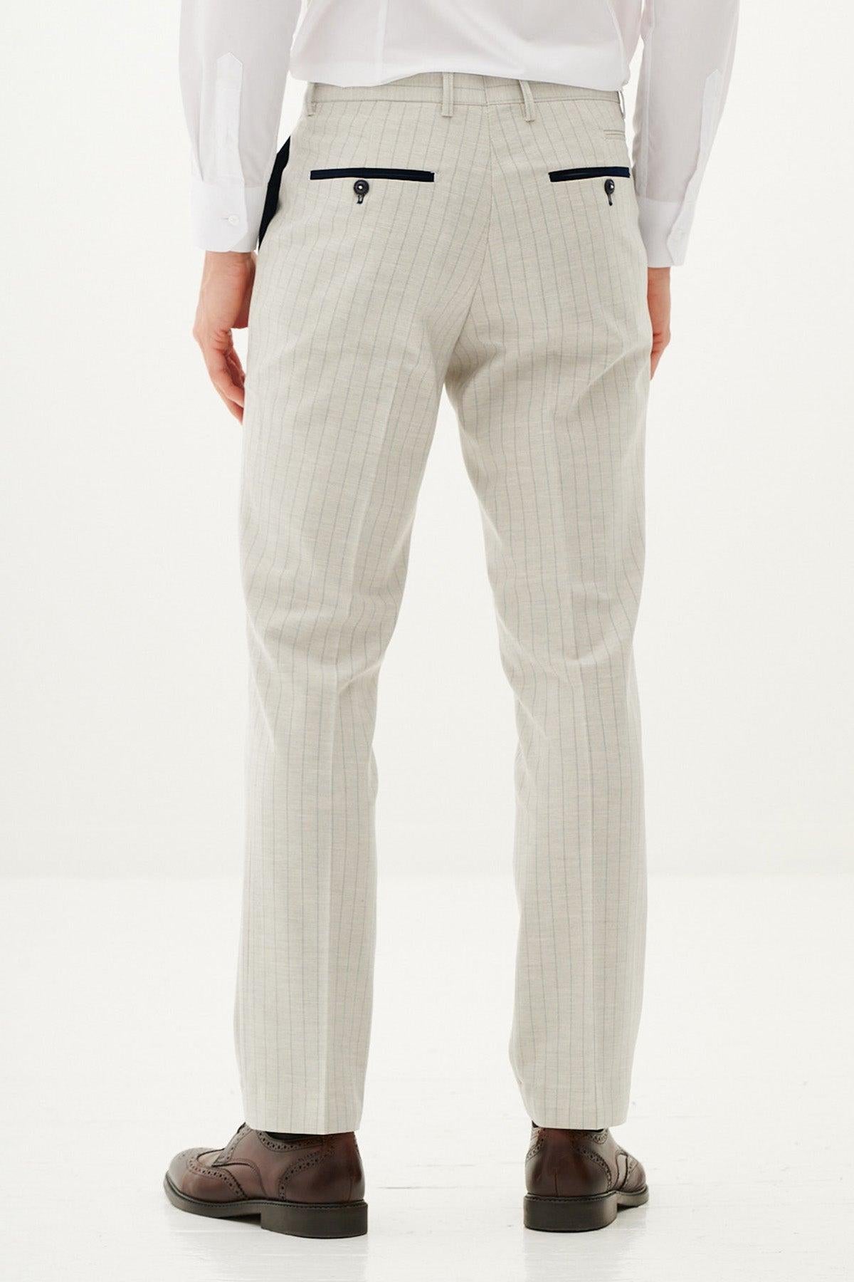 A person faces away, wearing Marc Darcy's GRANT - Stone Pinstripe Trousers with black buttoned back pockets, a white dress shirt, and brown dress shoes against a plain white background.