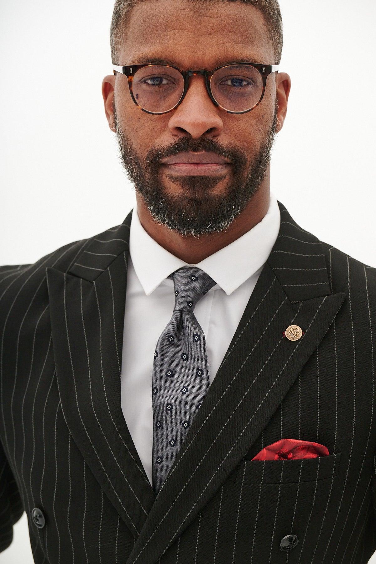 Man in the Marc Darcy ROCCO black pinstripe double breasted two piece suit, styled with glasses, a grey patterned tie, and a red pocket square.