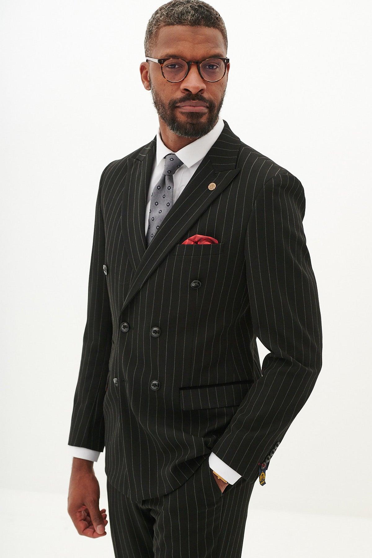 A Black man with glasses and a beard wears the Marc Darcy ROCCO Black Pinstripe Double Breasted Two Piece Suit in a tailored fit, styled with a gray tie, red pocket square, and gold lapel pin for a polished look.