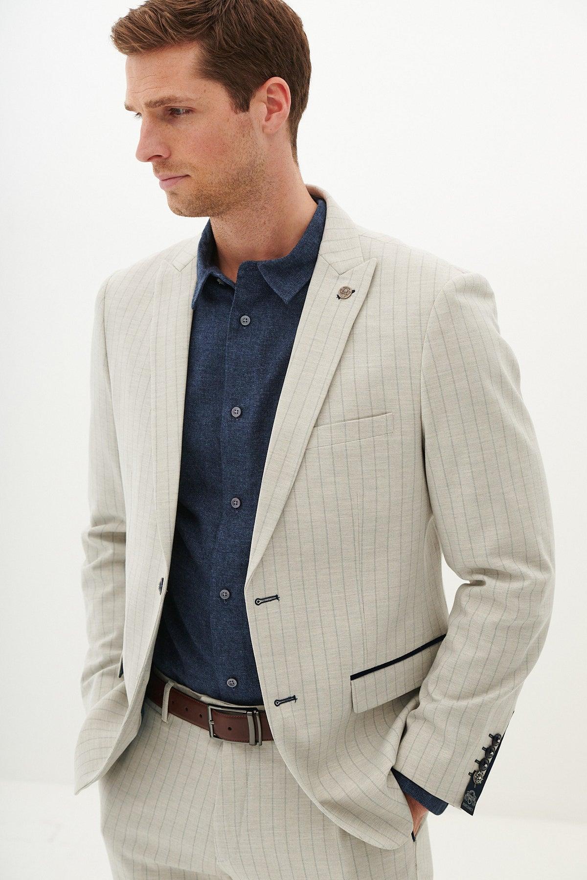 A man models the Marc Darcy GRANT Stone Pinstripe Two Piece Suit with a navy button-up shirt and brown leather belt, set against a white background.