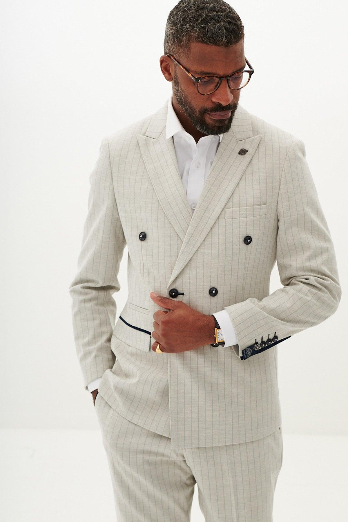 A man with short hair and a beard wears the Marc Darcy GRANT Stone Double Breasted Pinstripe Blazer over a white dress shirt, paired with glasses and a watch. He stands against a plain white background looking down to his left.