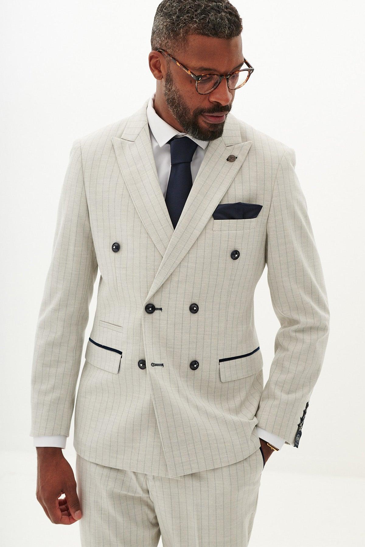A man in the Marc Darcy GRANT Stone Double Breasted Pinstripe Blazer with black buttons, a navy tie, white shirt, and glasses stands against a plain white background.
