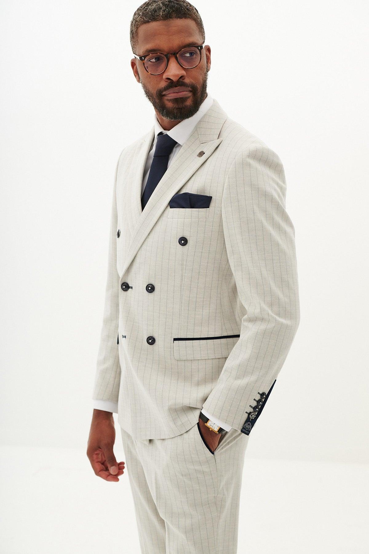 A man with short hair, a beard, and glasses wears the Marc Darcy GRANT Stone Pinstripe Double Breasted Suit with a navy tie and pocket square, standing against a plain white background.