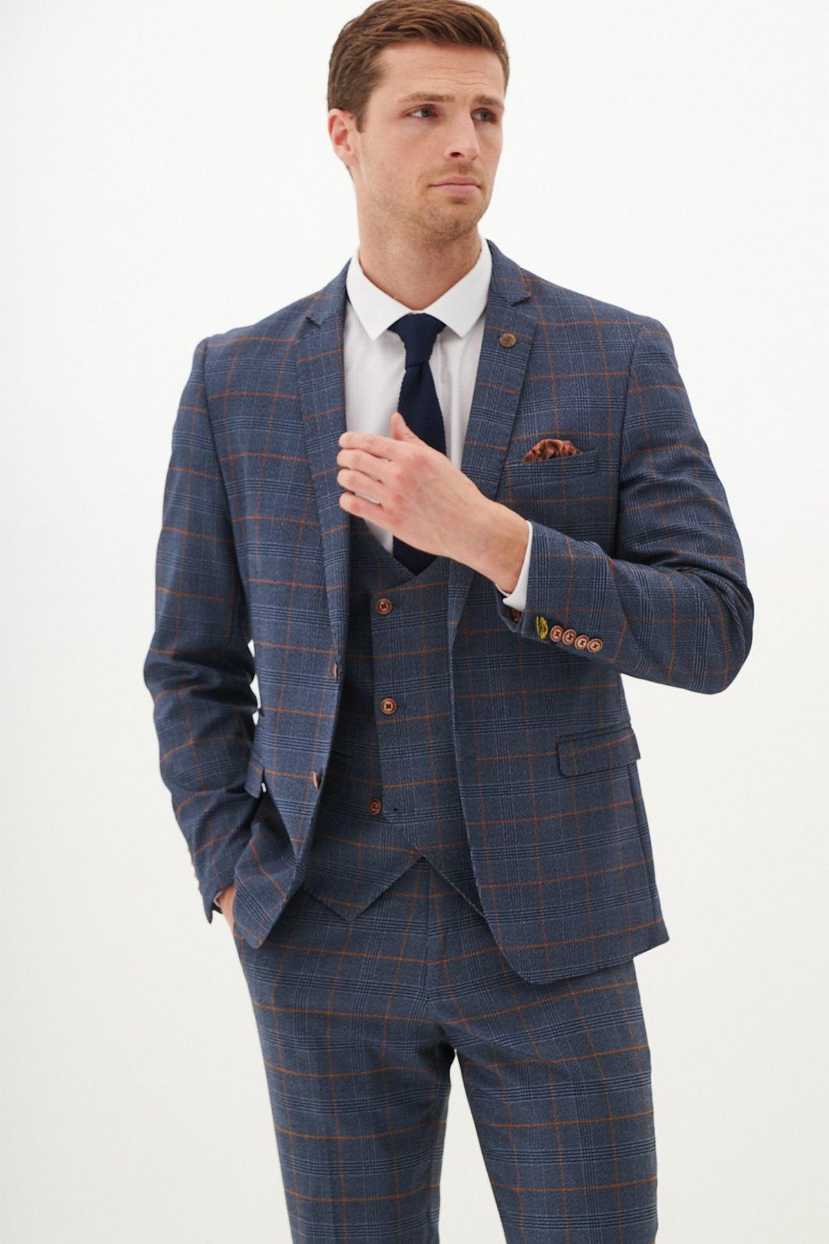A man in the marcdarcy JENSON Sky Blue Check Suit with Double Breasted Waistcoat, white shirt, dark tie, and pocket square stands against a white background, looking to the side with one hand touching his blazer.