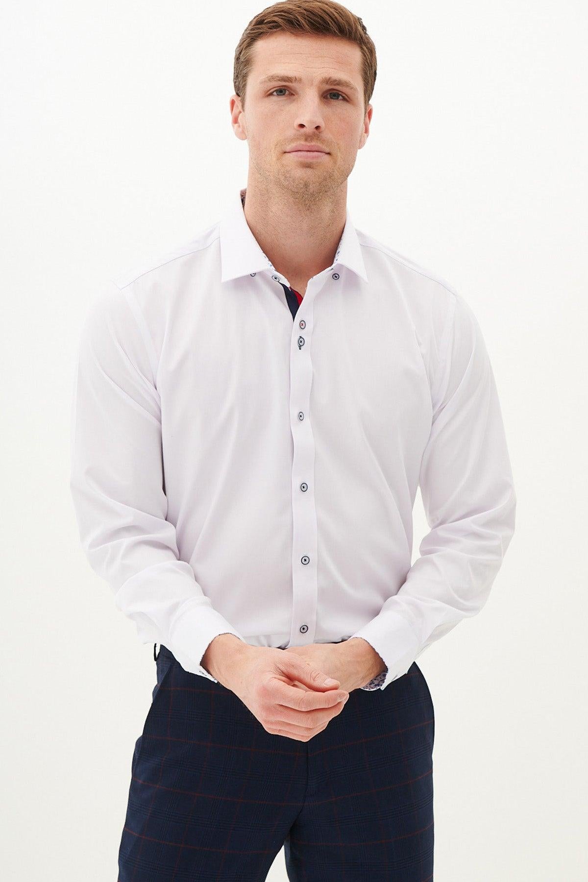 A man wearing the Marc Darcy LUKE white long sleeve shirt with subtle floral details and dark plaid pants stands against a plain, light background, hands clasped in front.
