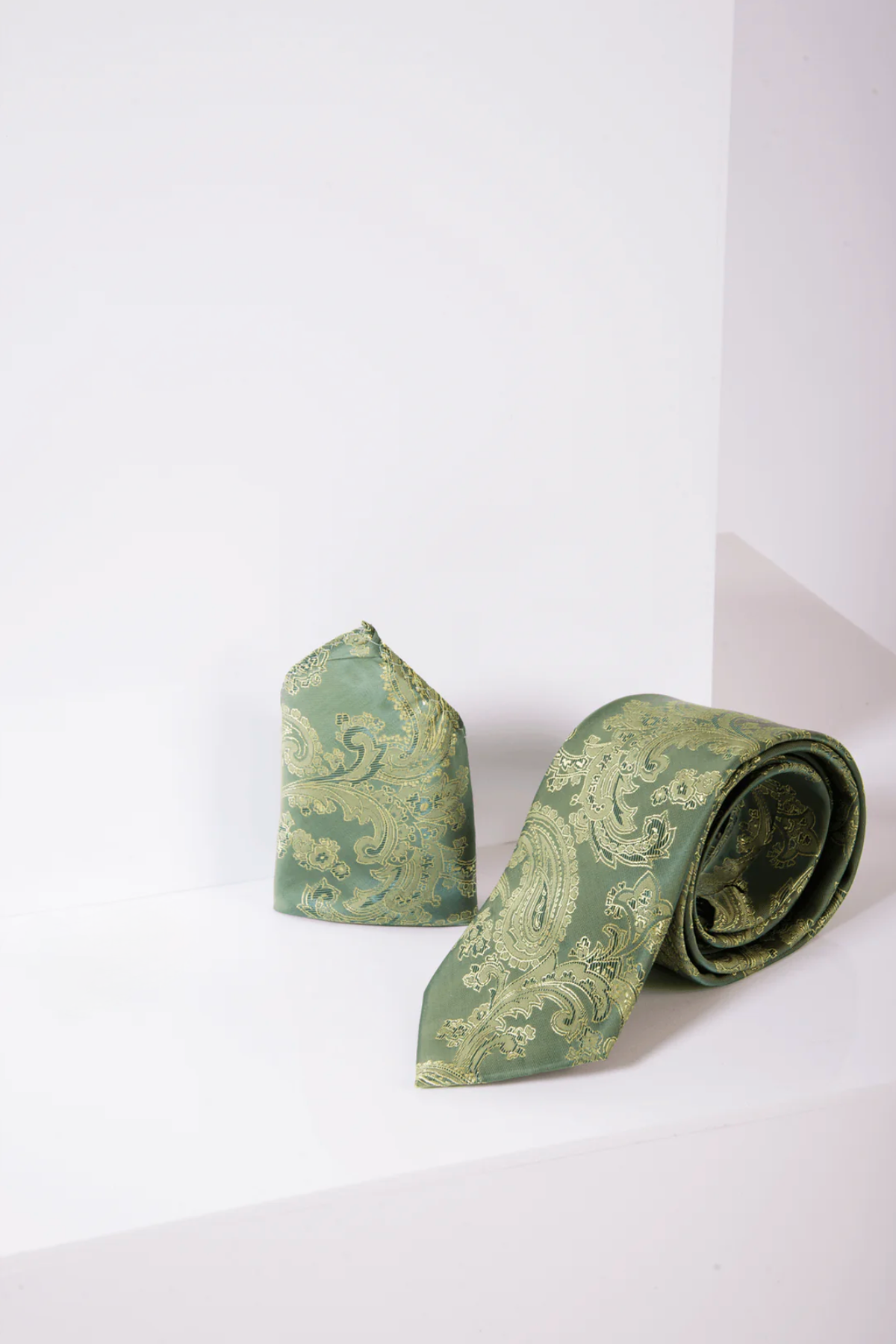 The Marc Darcy MD PAISLEY Green Paisley Tie and Pocket Square Set sits on a white geometric surface, making an ideal accessory for elevating formal outfits.