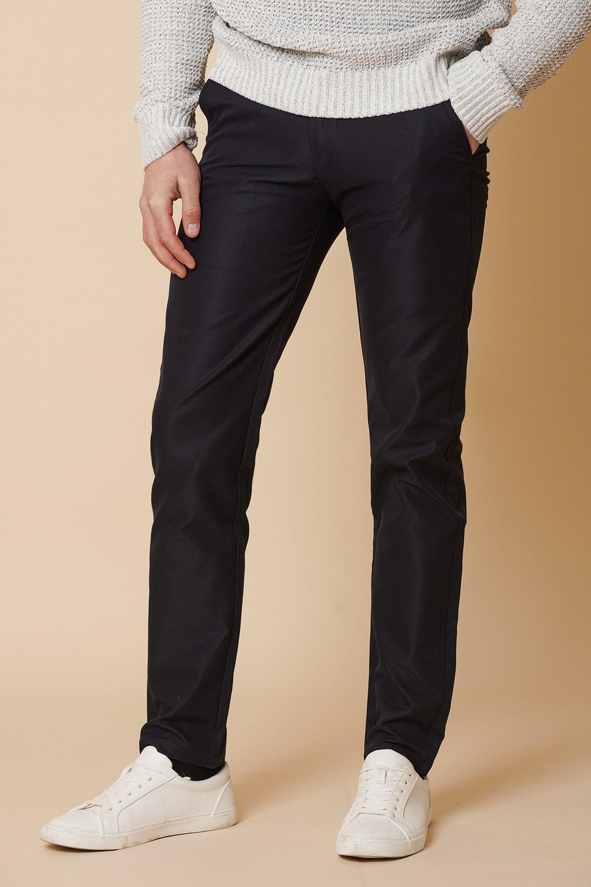 Only the lower body is visible: a person stands against a beige background, wearing marcdarcy's ENZO - Navy Chinos with a light gray sweater and white sneakers.
