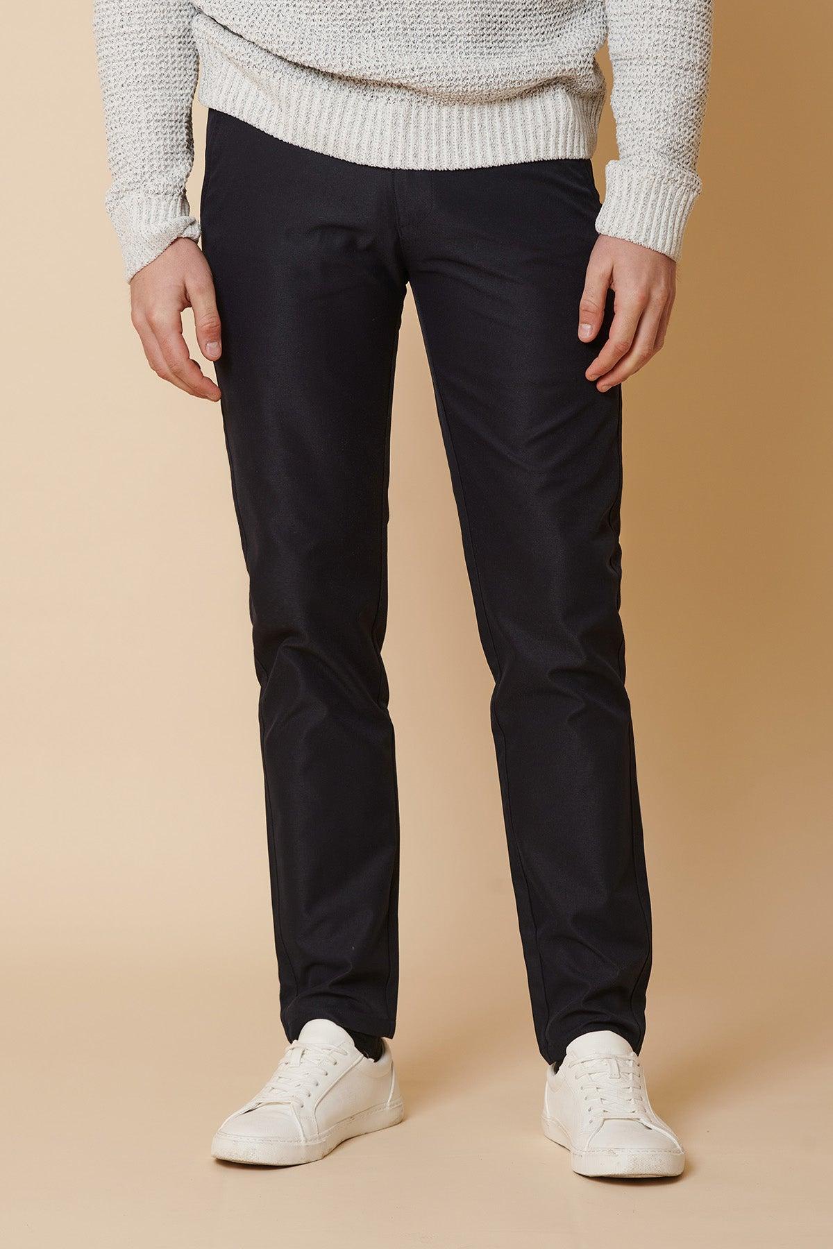 A person wearing a grey knit sweater, marcdarcy ENZO navy chinos, and white sneakers stands against a light tan background.