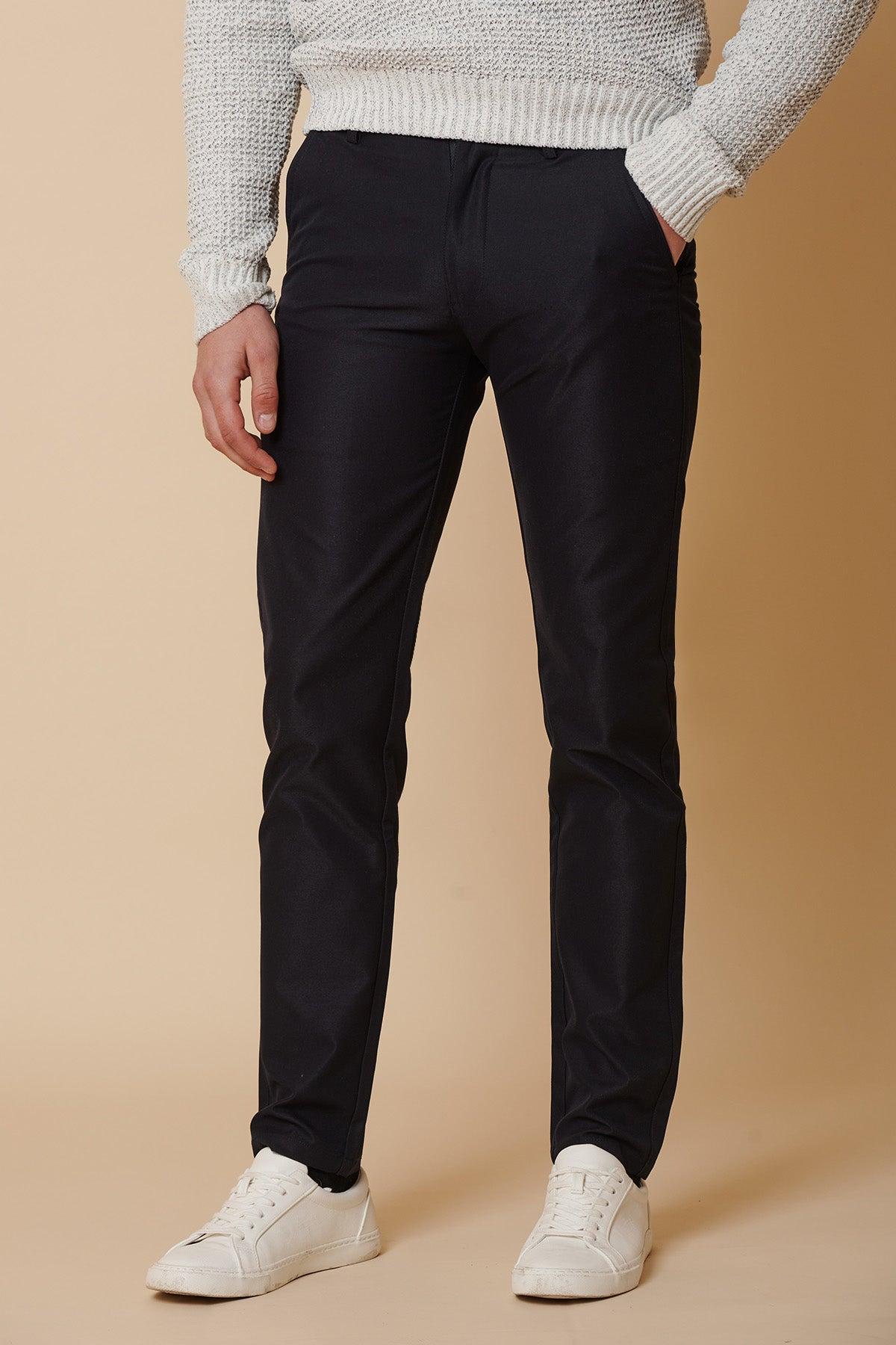 A person wears marcdarcy’s ENZO Navy Chinos with a light gray knit sweater and white sneakers, standing against a beige background. The image shows them from shoulders to feet.