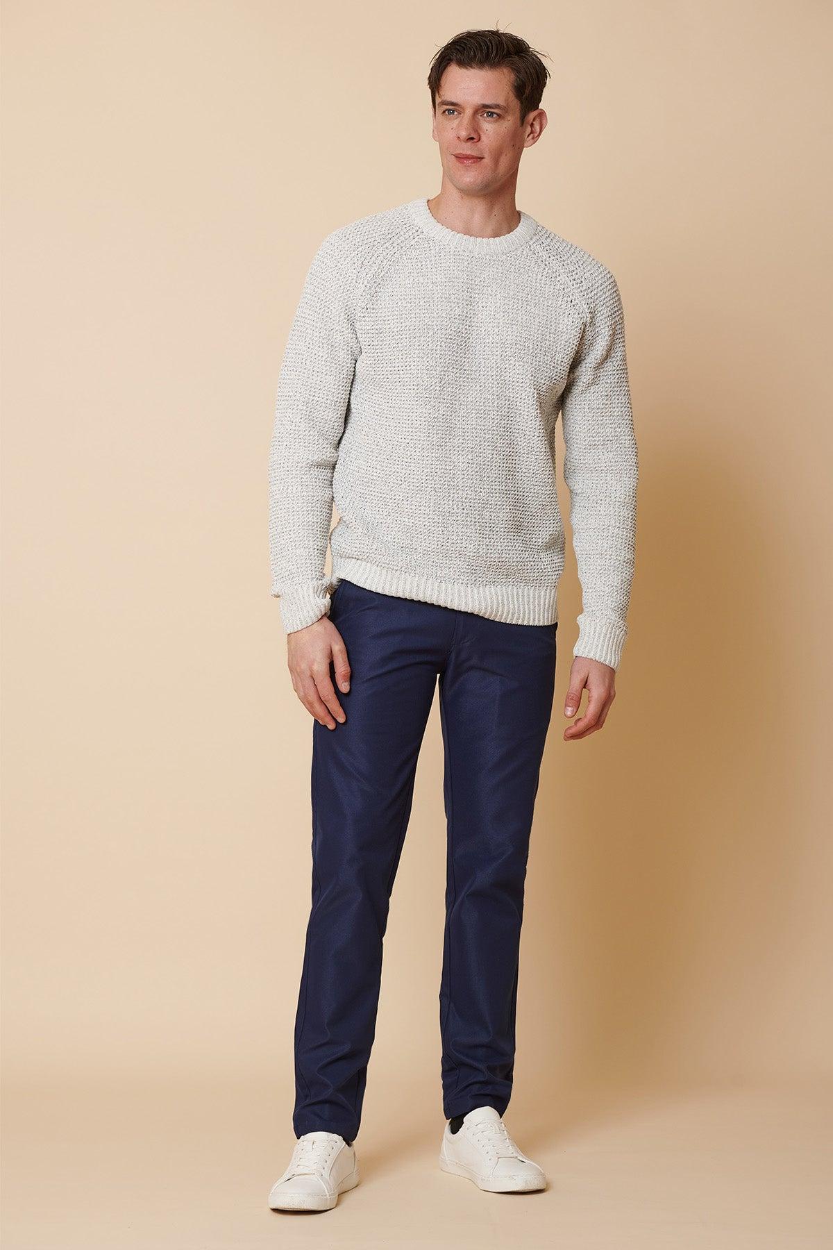 A man wears a light grey textured crewneck sweater, marcdarcy ENZO Royal Blue Chinos, and white sneakers against a beige background.