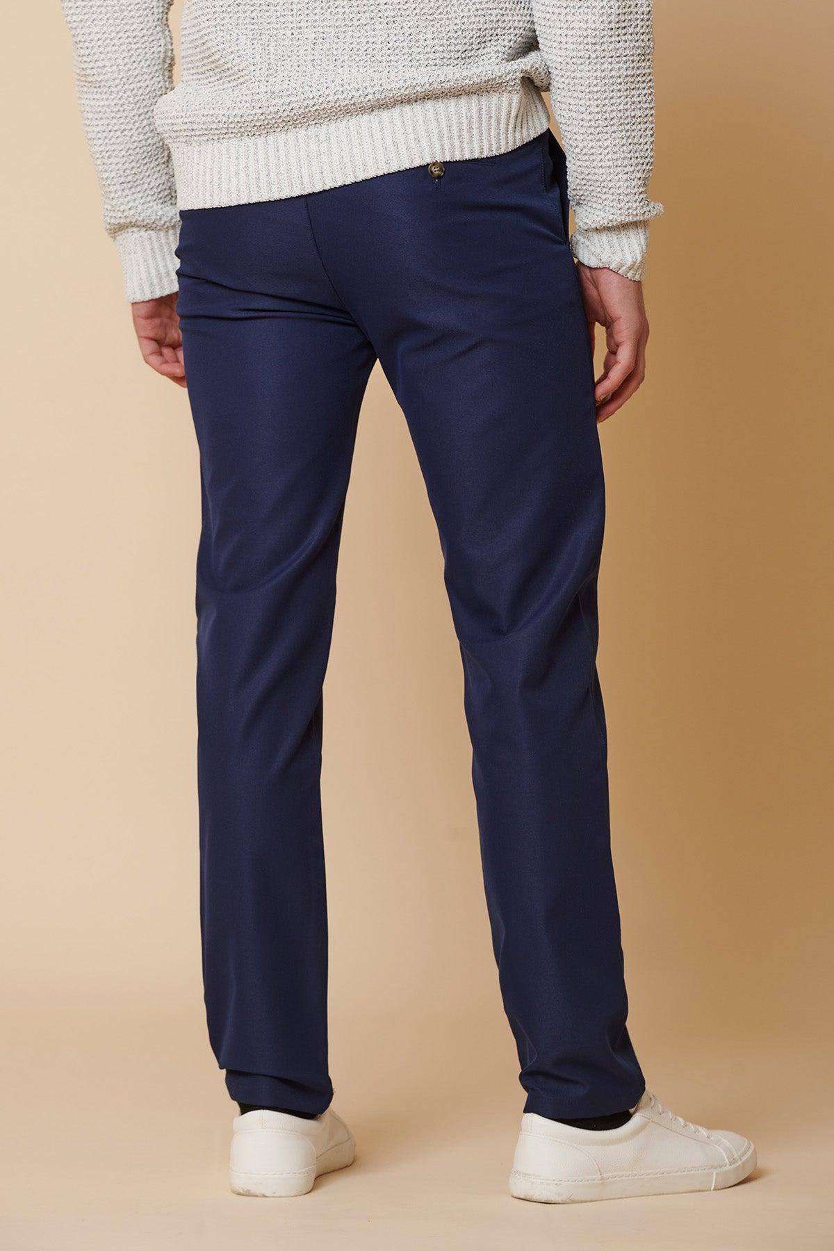 A person stands facing away against a beige background, wearing a white knit sweater, marcdarcy ENZO Royal Blue Chinos, and white sneakers.