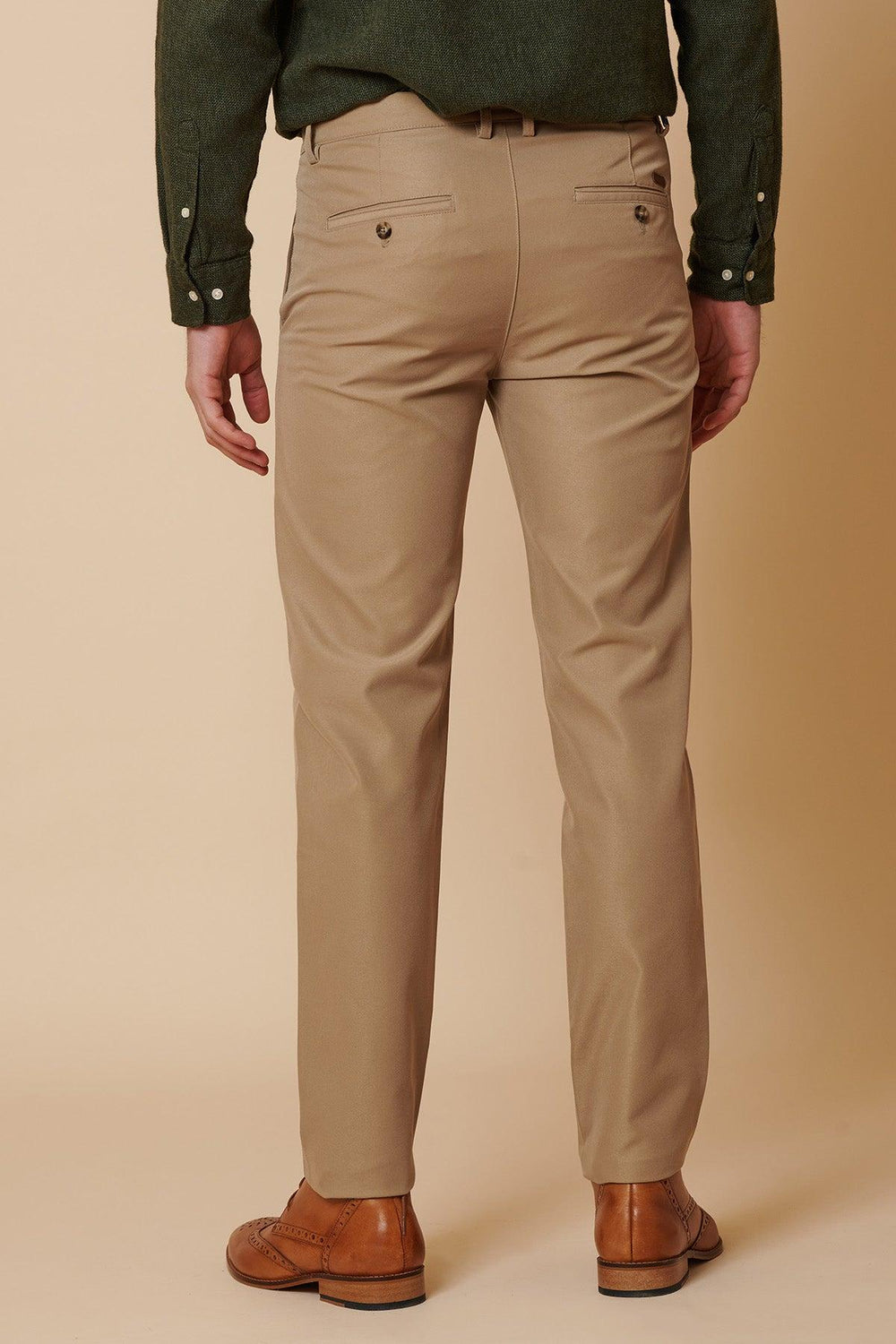 A person faces backward against a plain beige background, wearing marcdarcy ENZO - Sand Chinos, a dark green shirt, and brown dress shoes.