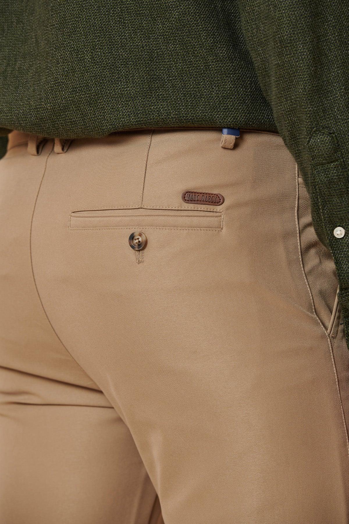A close-up of a person wearing the marcdarcy ENZO Sand Chinos, styled with a dark green textured shirt. These smart-casual chinos feature a buttoned back pocket and a small leather label above the pocket.