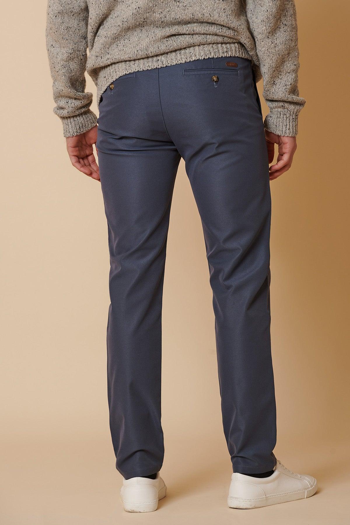 A person in marcdarcy ENZO Grey Blue Chinos, a gray textured sweater, and white sneakers stands with their back to the camera against a beige background.