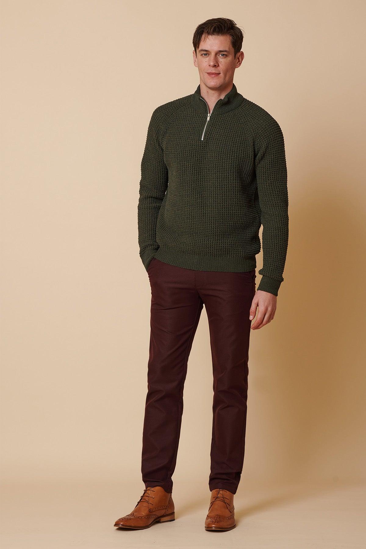 A man models marcdarcy's ENZO Wine Chinos and a green quarter-zip sweater in a studio photo.