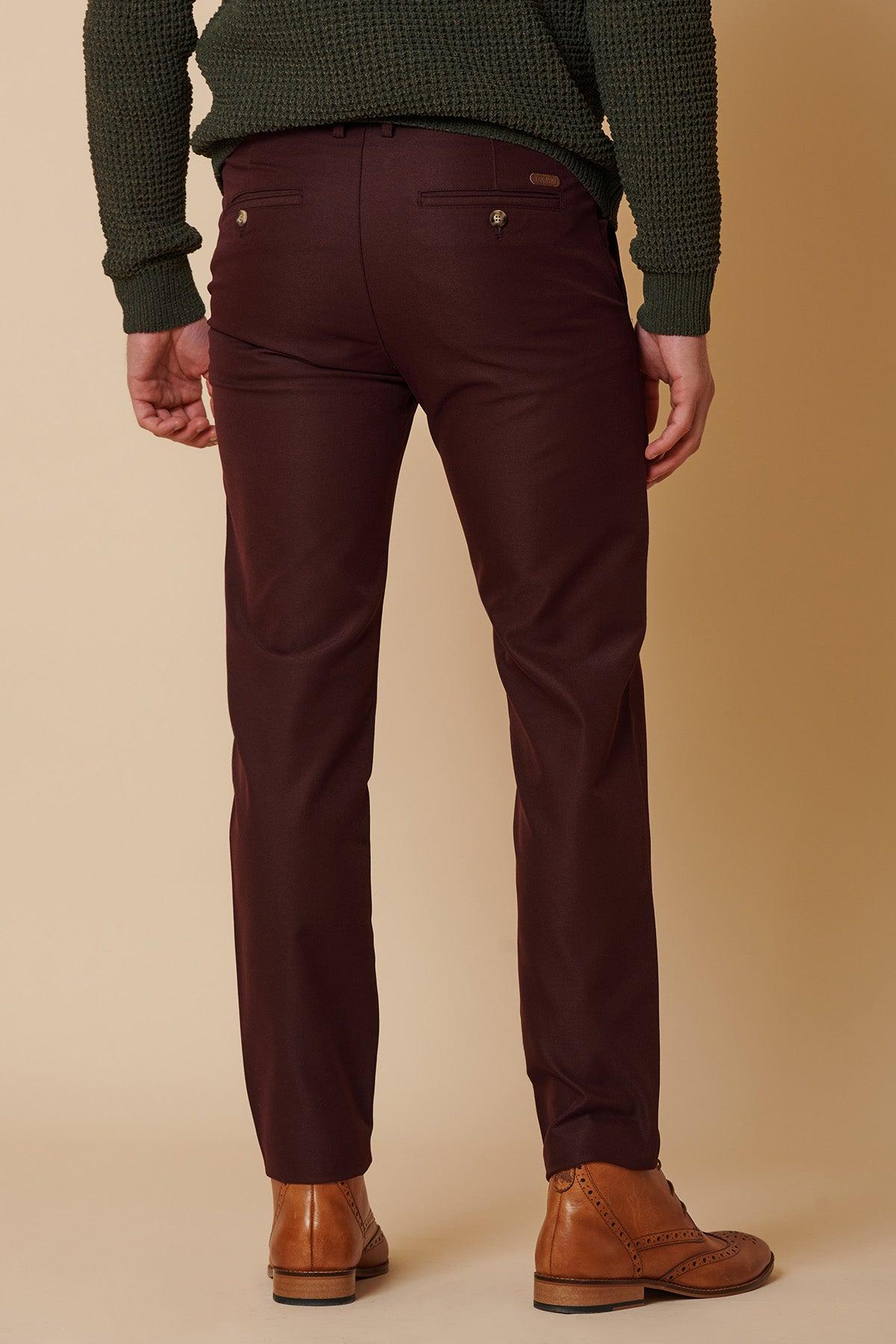 A person wearing marcdarcy ENZO Wine Chinos, a dark green textured sweater, and tan leather dress shoes stands with their back to the camera against a beige background.
