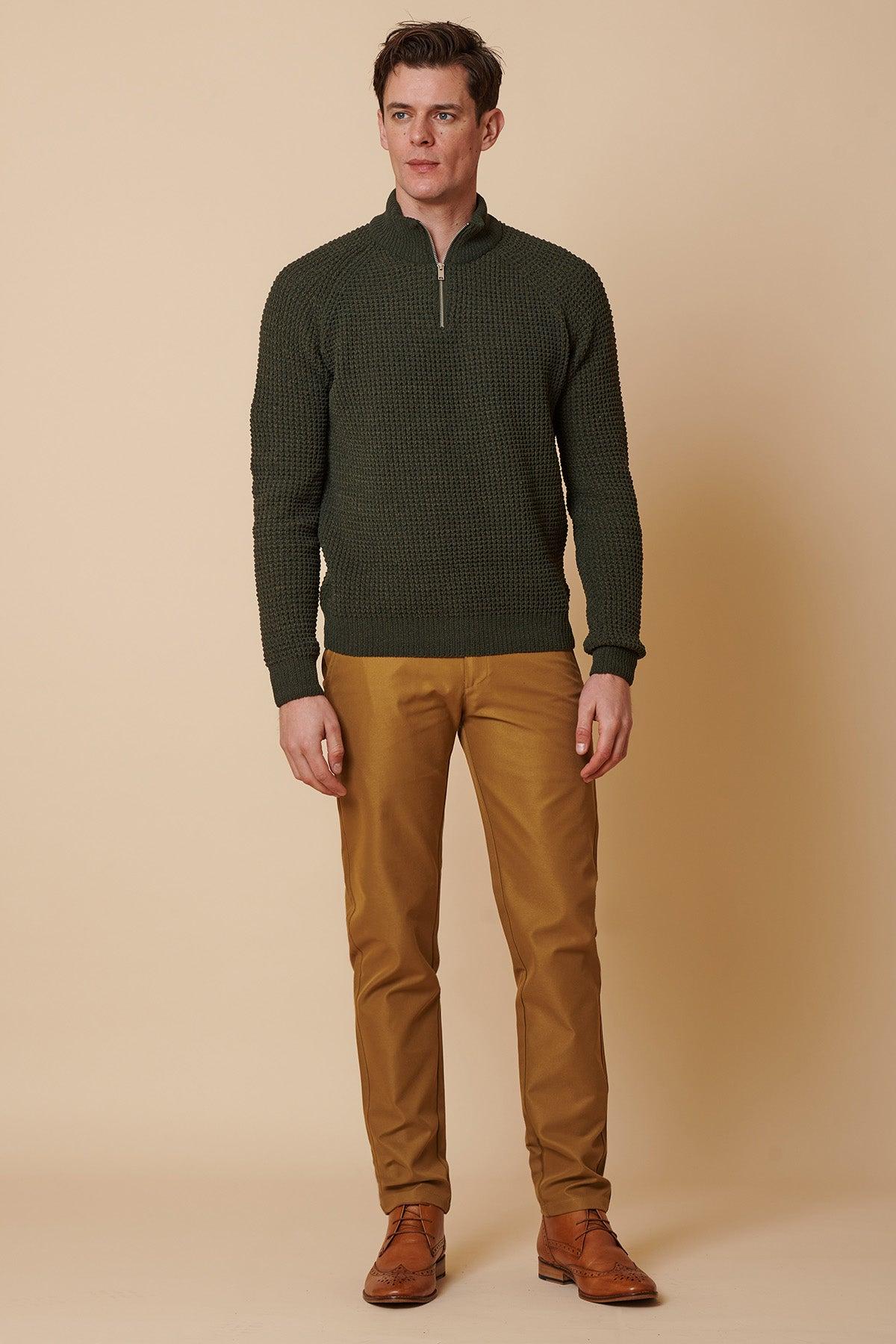 A man stands against a beige background wearing a dark green textured half-zip sweater, marcdarcy ENZO Tan Chinos, and brown dress shoes. He faces forward with a neutral expression.