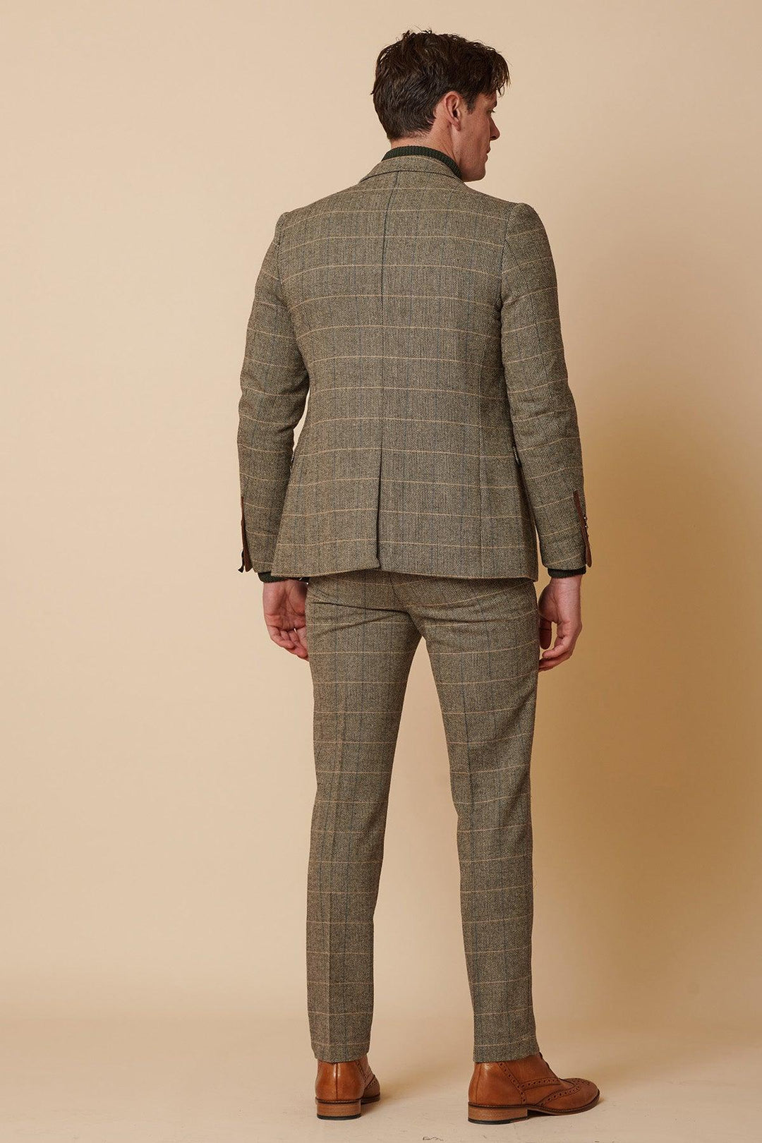 A man stands facing away, wearing the Marc Darcy TED - Tan Tweed Check Two Piece Suit with matching trousers and brown dress shoes, set against a beige background.