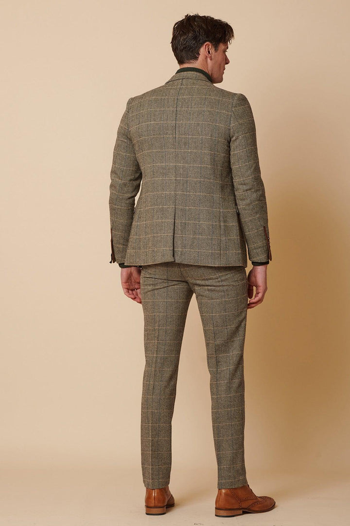 A man stands facing away, wearing the Marc Darcy TED - Tan Tweed Check Two Piece Suit with matching trousers and brown dress shoes, set against a beige background.