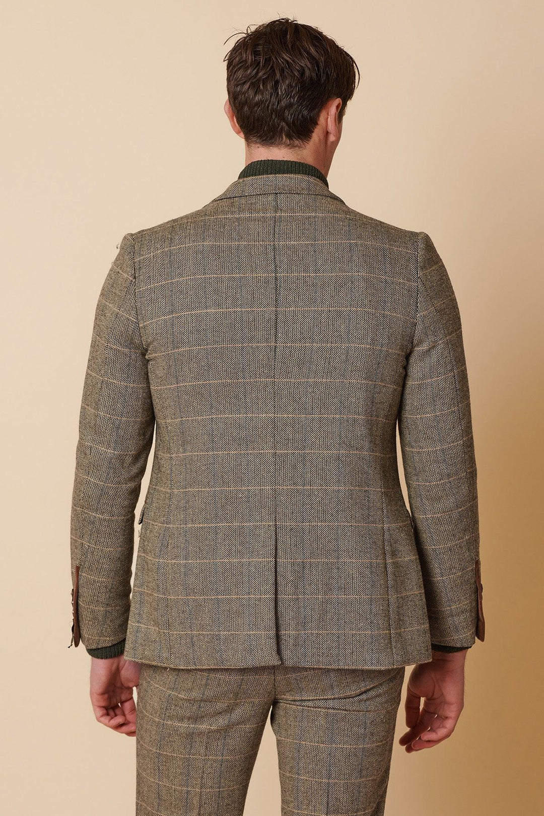 A man wearing the Marc Darcy TED Tan Tweed Check Two Piece Suit stands facing away from the camera, showcasing the back of his jacket and pants against a beige background.