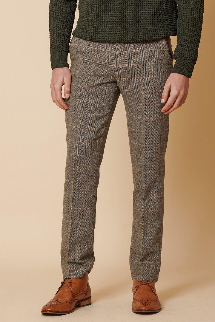 A person wears the marcdarcy DX7 - Tan Tweed Check Two Piece Suit, styled with brown plaid dress pants, a dark green textured sweater, and brown leather dress shoes, standing against a beige background. The person’s upper face is not visible.