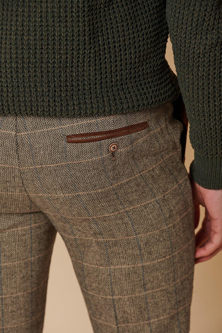 A person wearing marcdarcy's DX7 Tan Tweed Check Two Piece Suit, with brown plaid trousers featuring a leather-accented back pocket and button, paired with a dark green textured sweater—a perfect herringbone slim fit look.