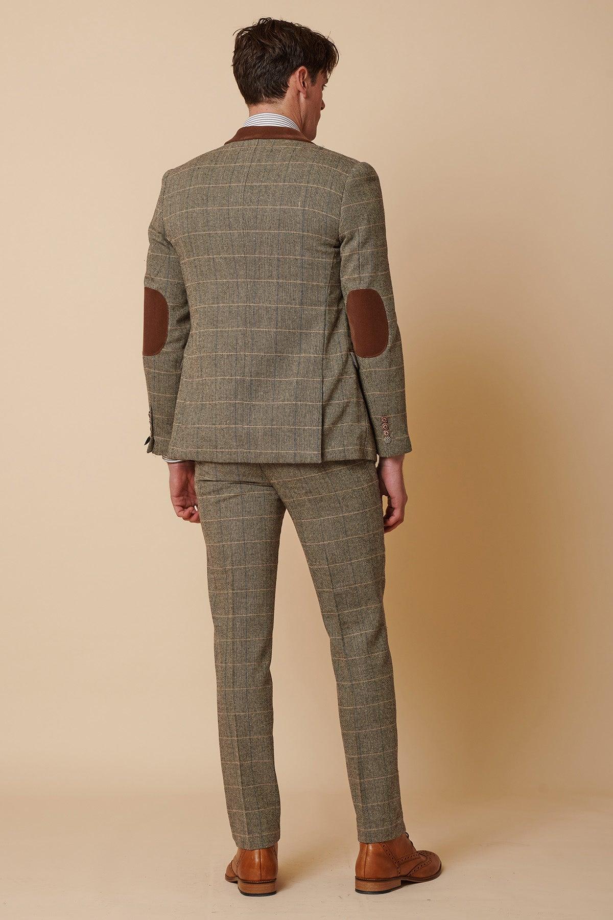 A man stands facing away, wearing the marcdarcy DX7 - Tan Tweed Check Two Piece Suit with brown dress shoes and leather collar accents, set against a beige background.
