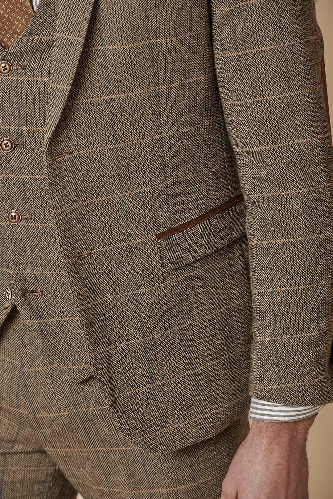 Close-up of a person wearing the Marc Darcy TED Tan Tweed Check Two Piece Suit, featuring a jacket and matching trousers. A striped shirt peeks out under the jacket, and their hand rests casually at their side.