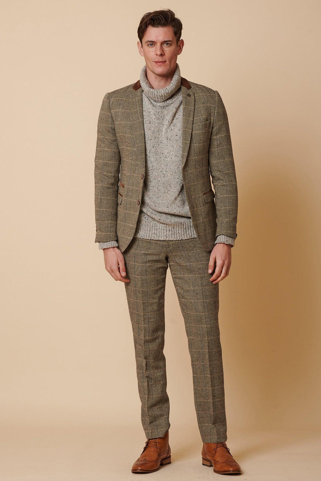 A man with short brown hair and a neutral expression stands against a beige background, dressed in the marcdarcy DX7 - Tan Tweed Check Two Piece Suit, paired with a light gray turtleneck sweater and brown dress shoes.