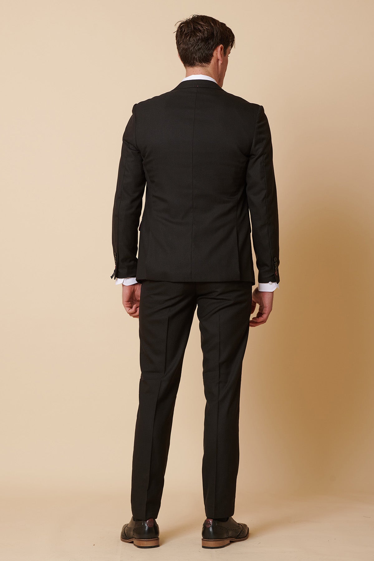 Man seen from behind in the DANNY Black Three Piece Suit With Single Breasted Waistcoat by Marc Darcy, paired with a crisp white shirt and brown shoes—a timeless formal menswear look.