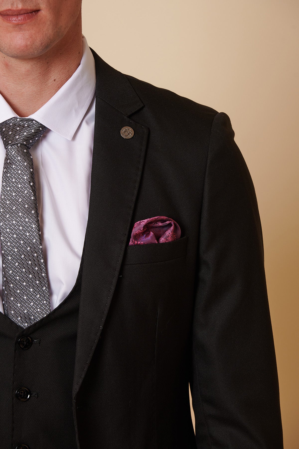 A man in a Marc Darcy DANNY Black Tailored Blazer, white shirt, patterned gray tie, and purple pocket square stands against a beige background, with only his upper left half visible.
