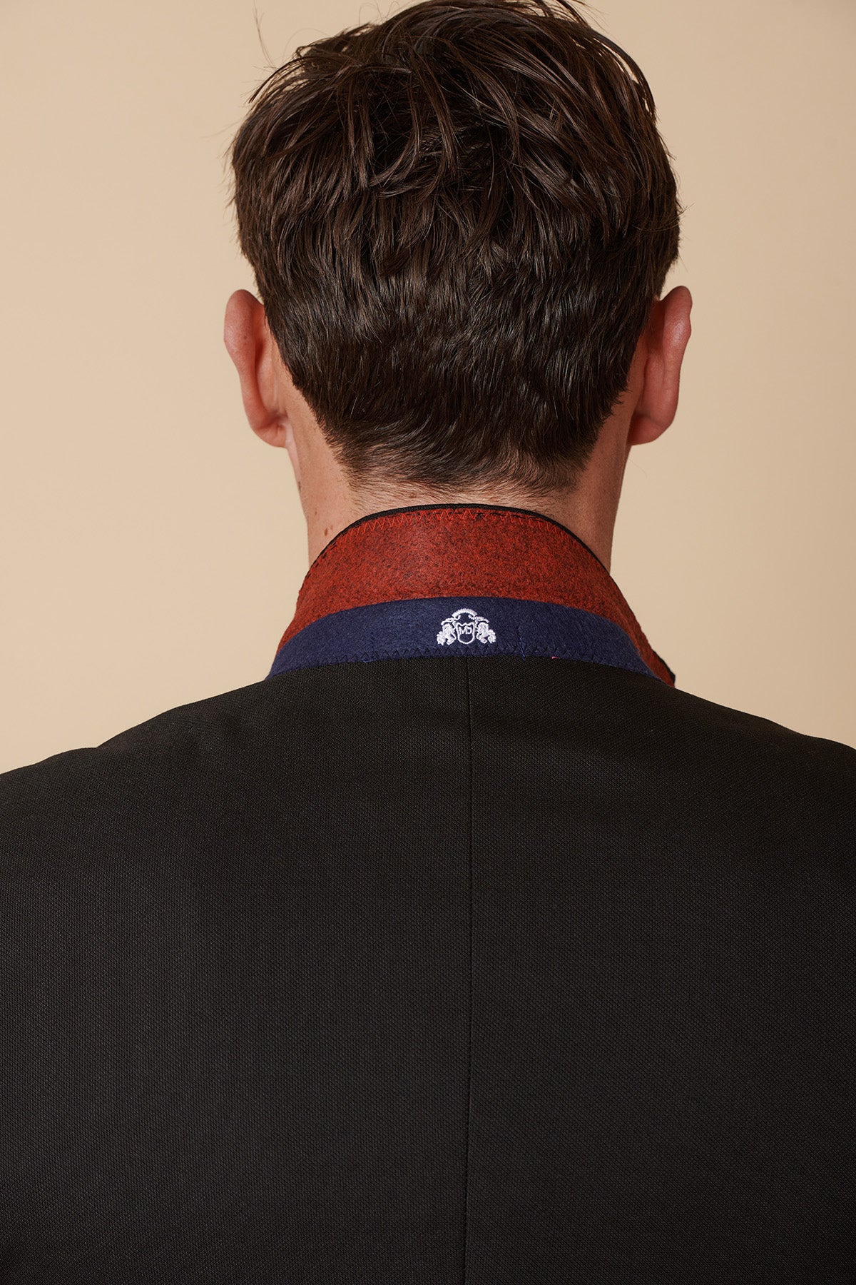 A man seen from behind wears the Marc Darcy DANNY black three piece suit with single breasted waistcoat, featuring a raised collar, red and blue lining, and a small white embroidered emblem—ideal for formal events or black tie dress codes.