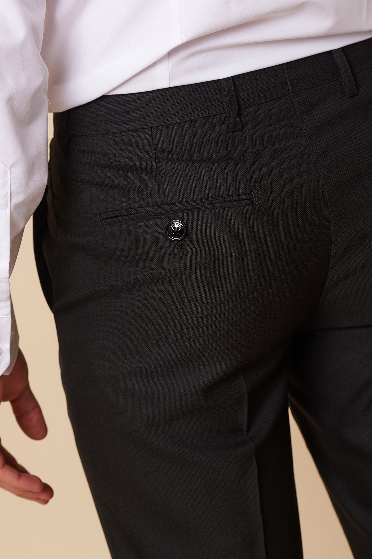 A close-up shows a person wearing Marc Darcys DANNY - Black Tailored Trousers and a white shirt, focusing on the back pocket with a black button. The left hand is partially visible, highlighting modern office style.