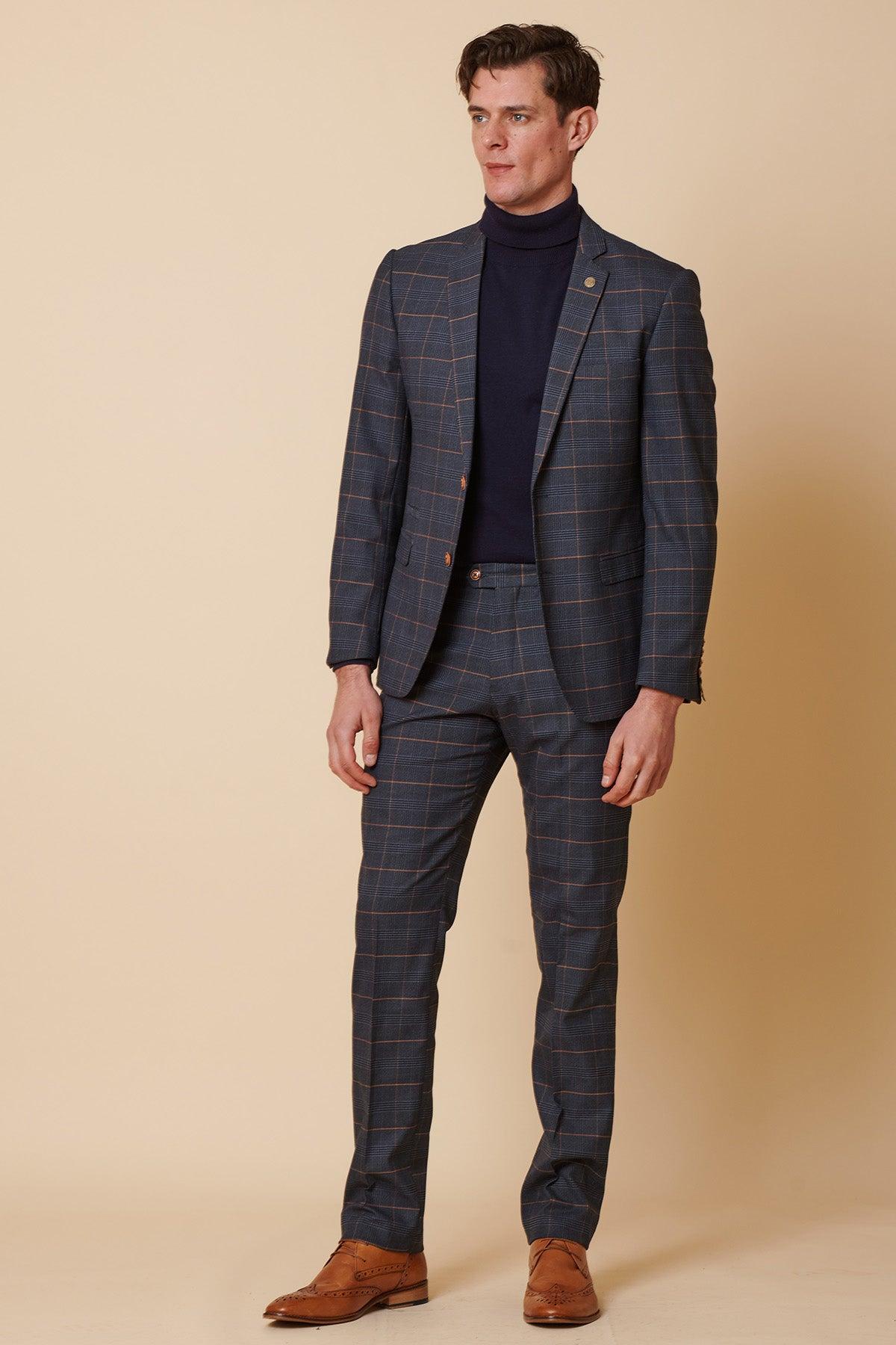 A man stands against a beige background wearing the Marc Darcy JENSON - Marine Navy Check Two Piece Suit, paired with a navy turtleneck and brown dress shoes.