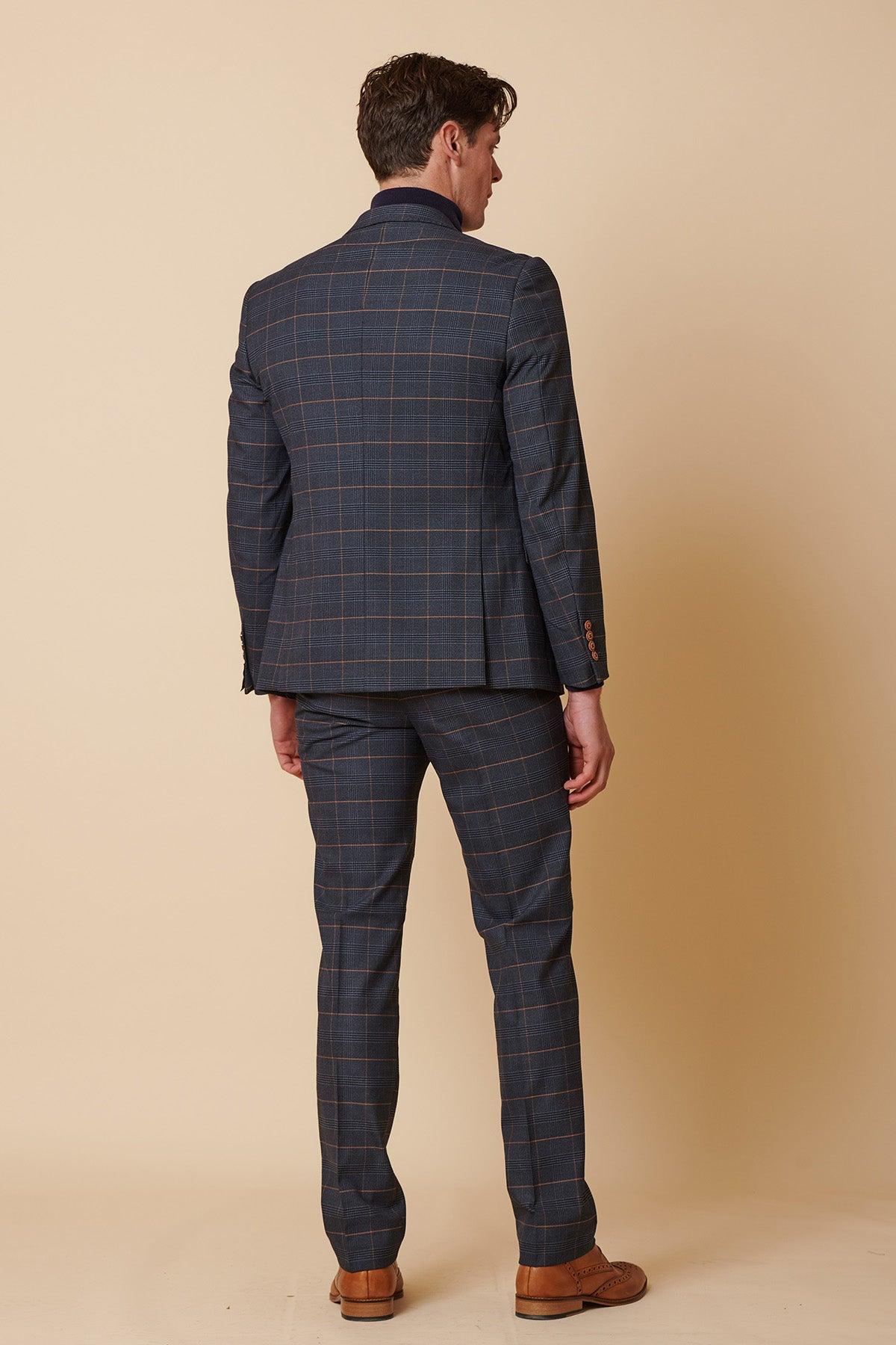 A man stands with his back to the camera in a Marc Darcy JENSON - Marine Navy Check Two Piece Suit and brown dress shoes, set against a plain beige background.