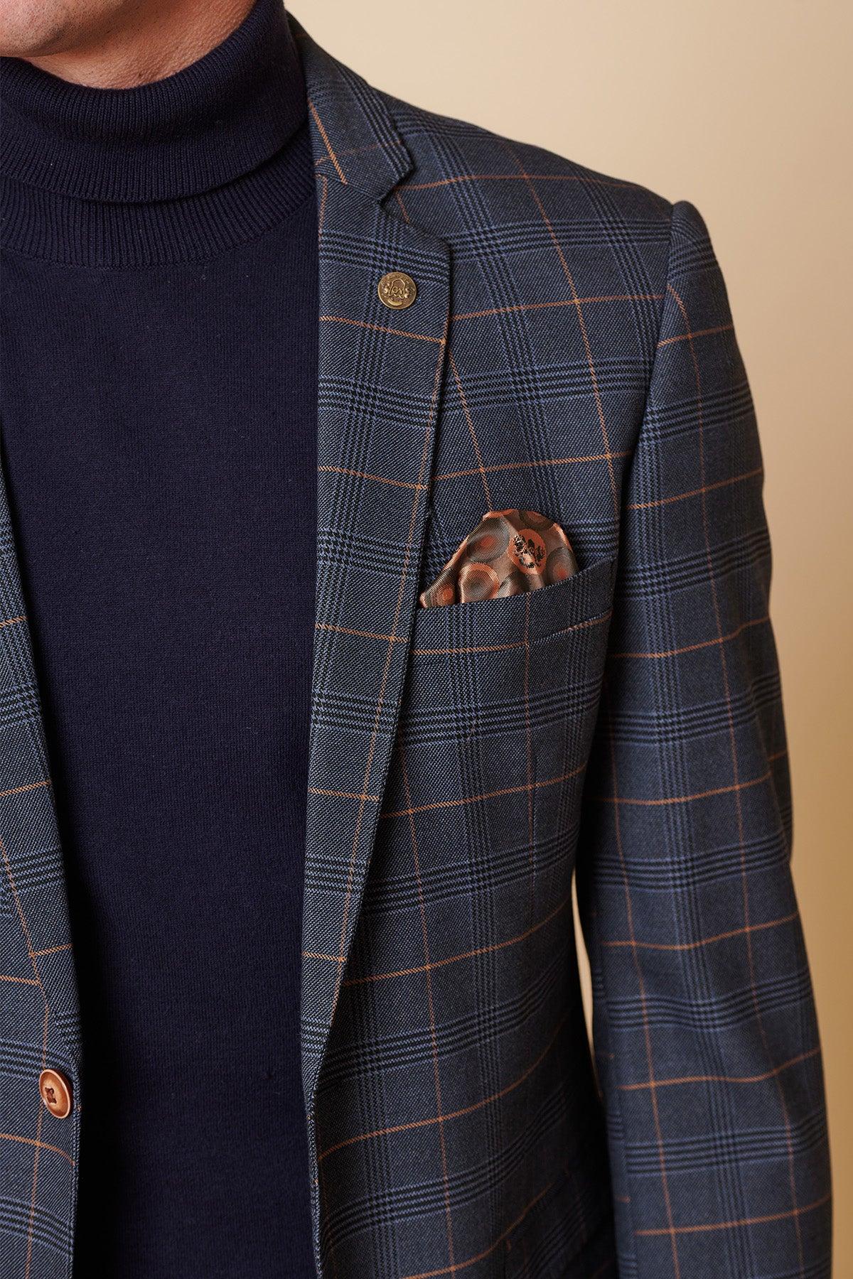 A man wears the Marc Darcy JENSON - Marine Navy Check Two Piece Suit, featuring a slim-fit blue plaid blazer with brown stripes and accents, photographed from shoulders to mid-torso against a beige background.