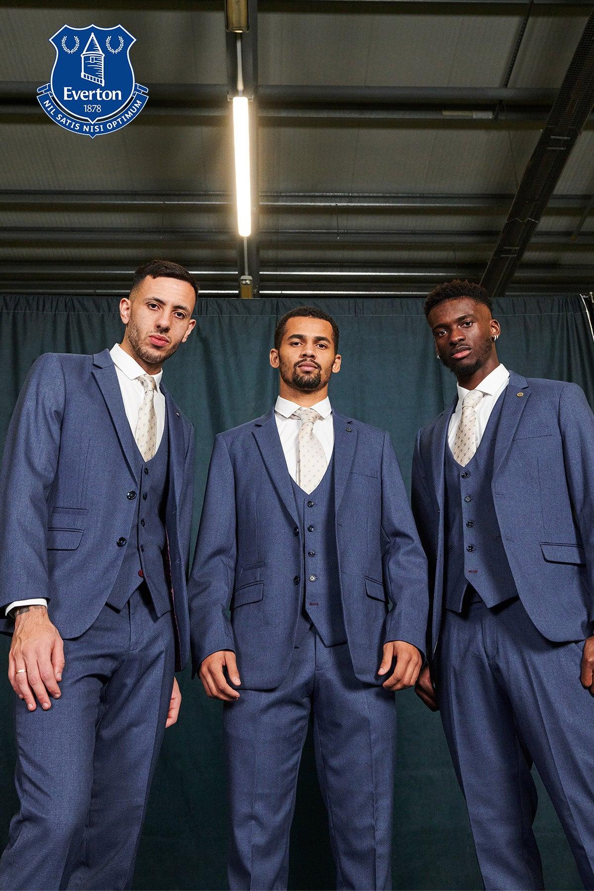 Three men in matching Marc Darcy ASHLEY Navy Blue Three Piece Suits from The Everton Collection stand confidently before a dark curtain, viewed from below. The Everton F.C. logo appears at the top left of the image.