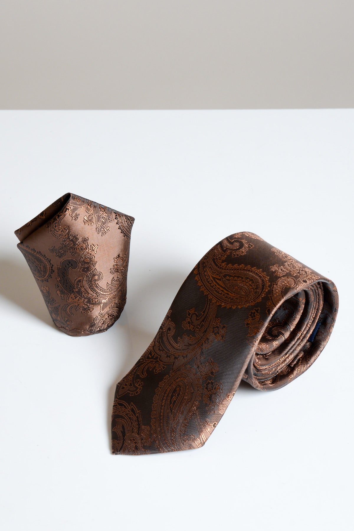 The Accessory MD PAISLEY set features a brown paisley print tie and matching pocket square, both elegantly displayed on a white surface.