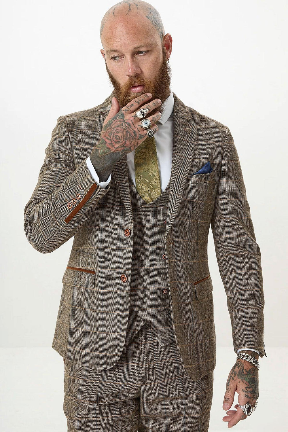 A bearded man with tattoos and multiple rings stands against a white background, wearing the marcdarcy TED Tan Tweed Check Three Piece Suit with Double Breasted Waistcoat, paired with a gold patterned tie and white shirt.