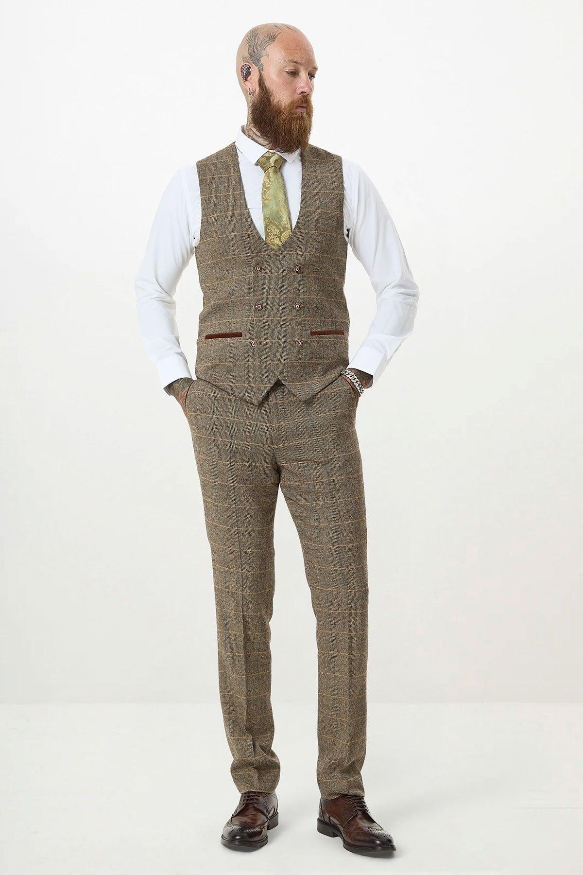 A bearded man stands in a neutral pose, wearing the marcdarcy TED Tan Tweed Check Double Breasted Waistcoat with a slim fit checked brown three-piece suit, white dress shirt, green tie, and brown shoes against a plain white background.
