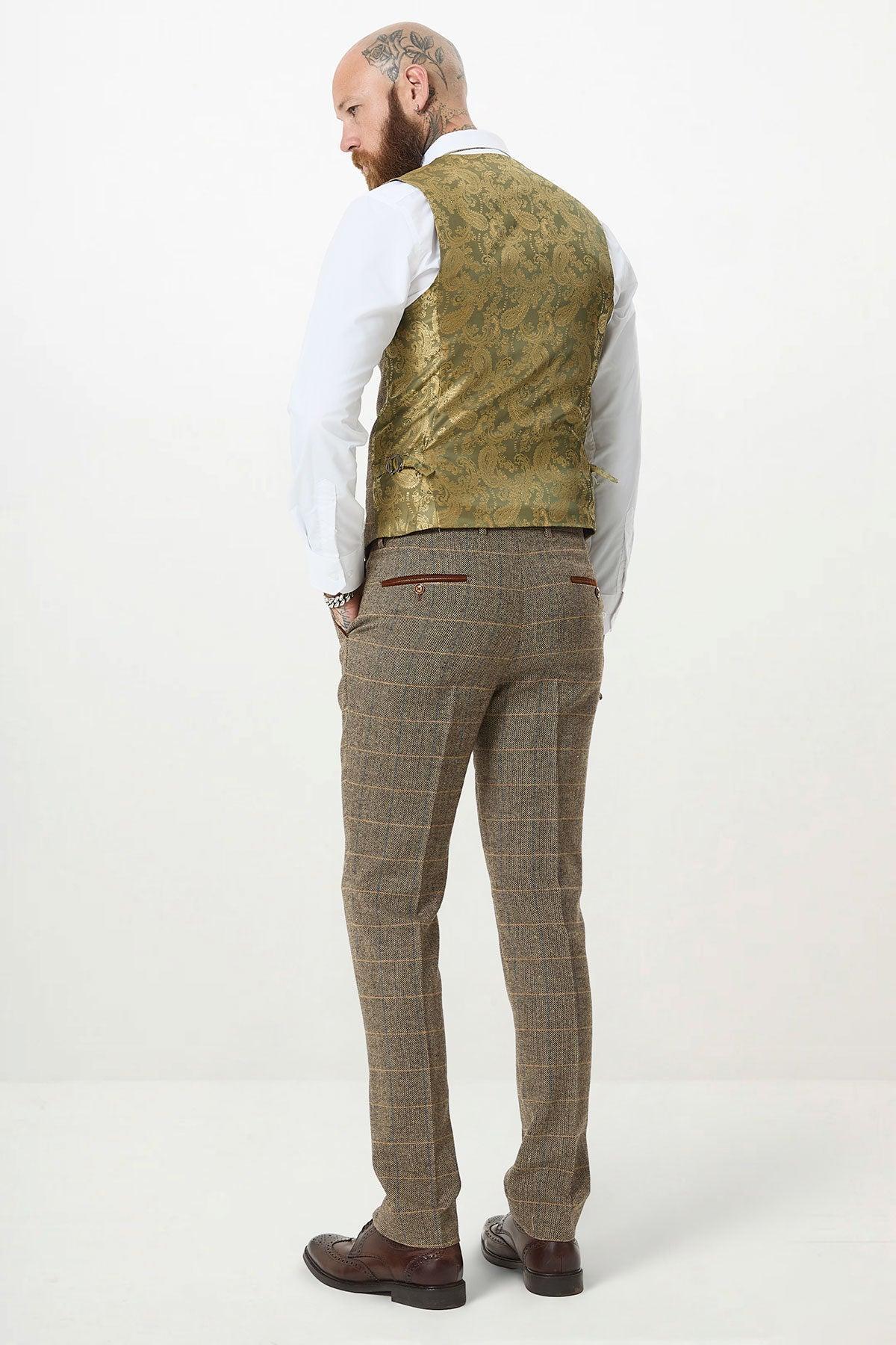 A man with tattoos on his shaved head and neck wears a slim fit white shirt, marcdarcy's TED Tan Tweed Check Double Breasted Waistcoat, brown plaid trousers, and brown shoes, standing with his back to the camera against a plain white background.
