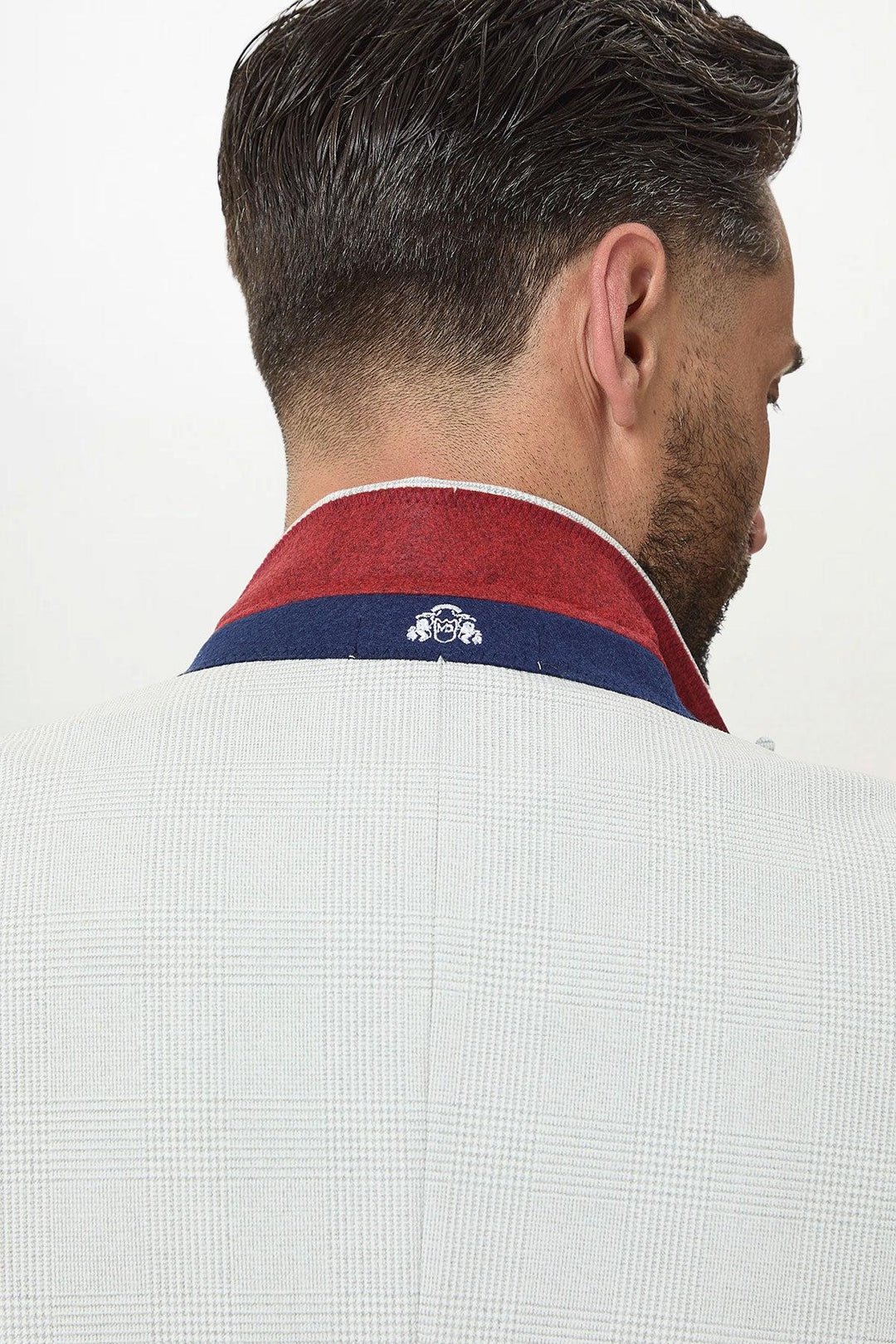 A man with short, dark hair is shown from behind wearing the Marc Darcy BROMLEY - Stone Check Suit with Kelvin Navy Waistcoat. The popped collar reveals a red and blue inner lining featuring a small white emblem.