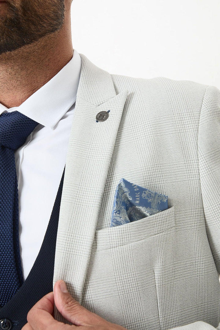 A man wears a Marc Darcy BROMLEY stone check suit with a Kelvin navy waistcoat, white shirt, and navy tie. A blue patterned pocket square is in his breast pocket. Only his lower face and upper torso are visible.