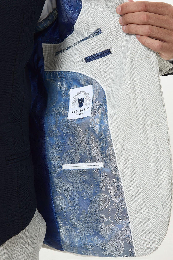 A person holds open a BROMLEY - Stone Check Suit jacket by Marc Darcy, revealing a blue paisley lining and a Marc Darcy label stitched inside the inner pocket.