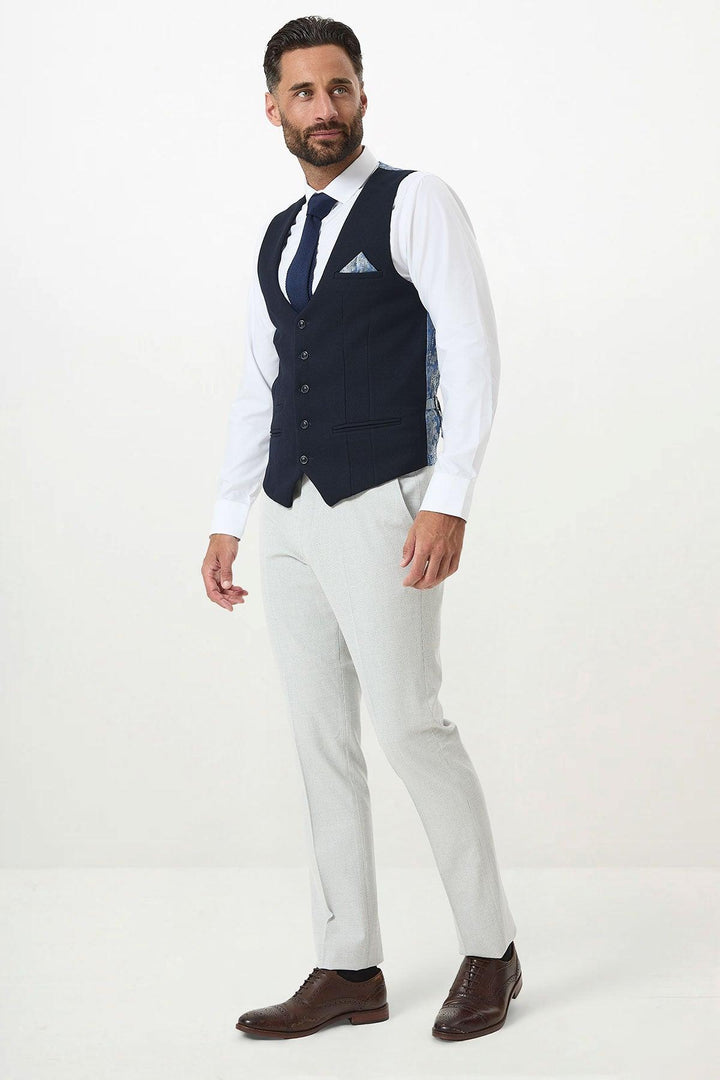 A man wears the Marc Darcy BROMLEY Stone Check Suit with Kelvin Navy Waistcoat, white shirt, patterned tie, brown leather shoes, and pocket square while standing against a plain white background.