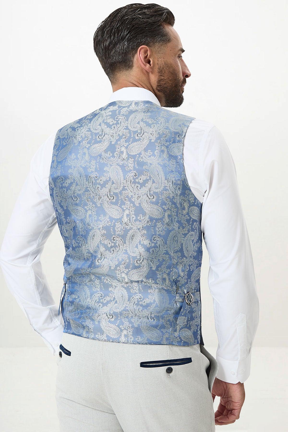 A man is seen from the back wearing marcdarcy’s KELVIN Sky Blue Single Breasted Waistcoat, featuring an intricate silver paisley pattern, paired with a white shirt and light gray trousers.