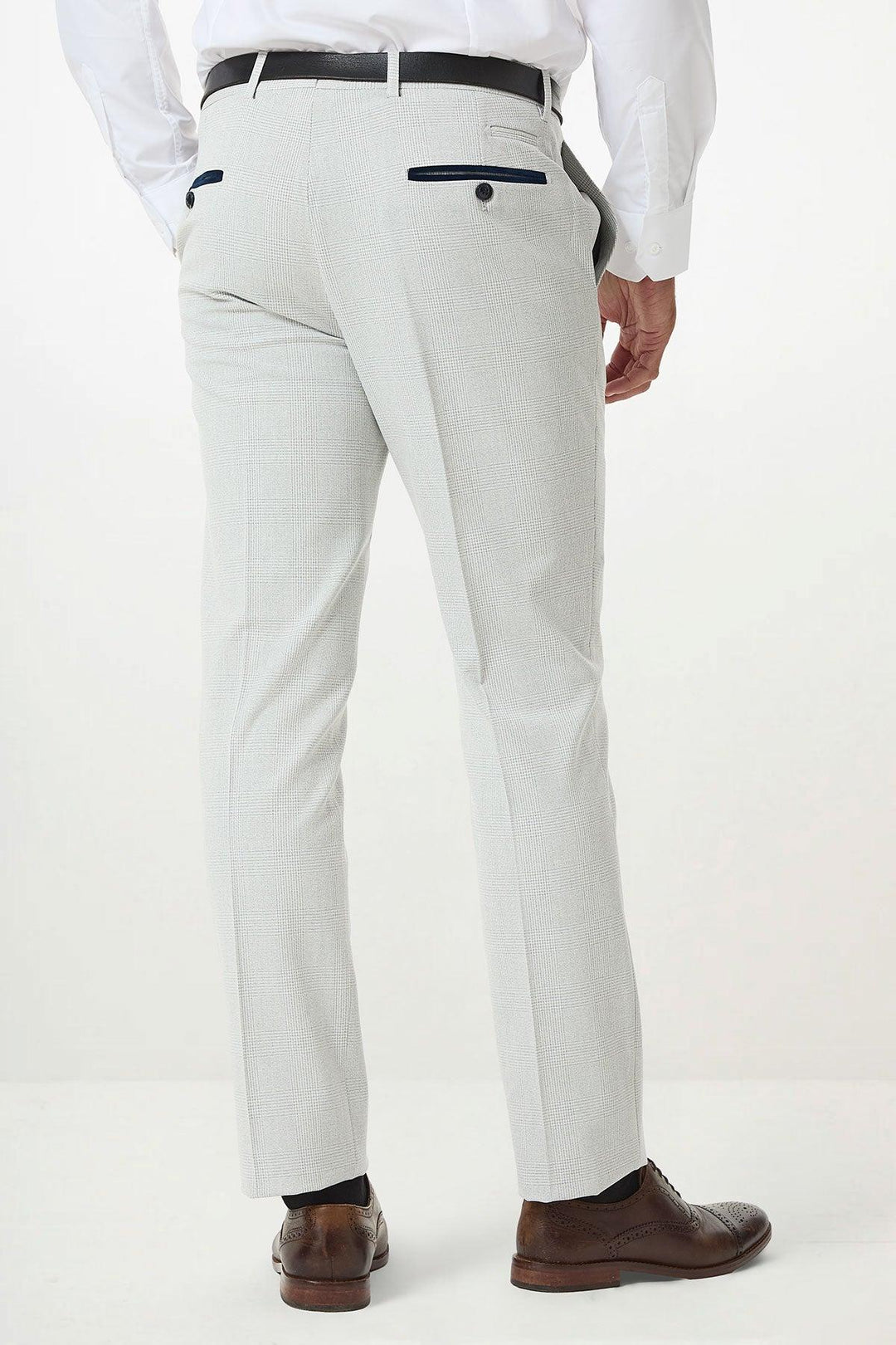 A man wearing Marc Darcys BROMLEY Stone Check Suit pants and a white shirt stands facing away; the light gray checked trousers feature black trim on the back pockets.