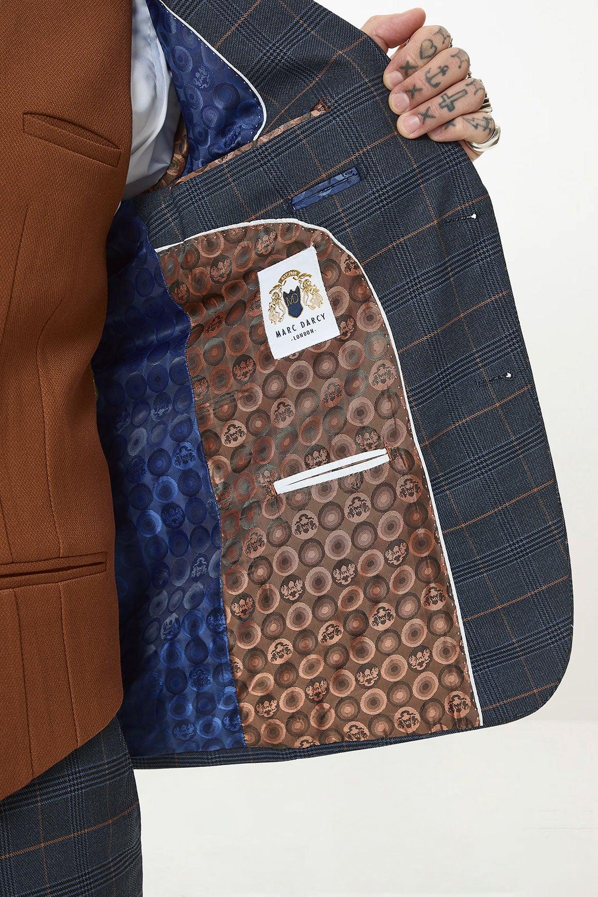 A person with tattooed fingers holds open a marcdarcy JENSON Marine Navy Check Suit with Kelvin Tan Waistcoat, showing the brown lining and distinctive inner fabric patterned with brown circles and a marcdarcy label.